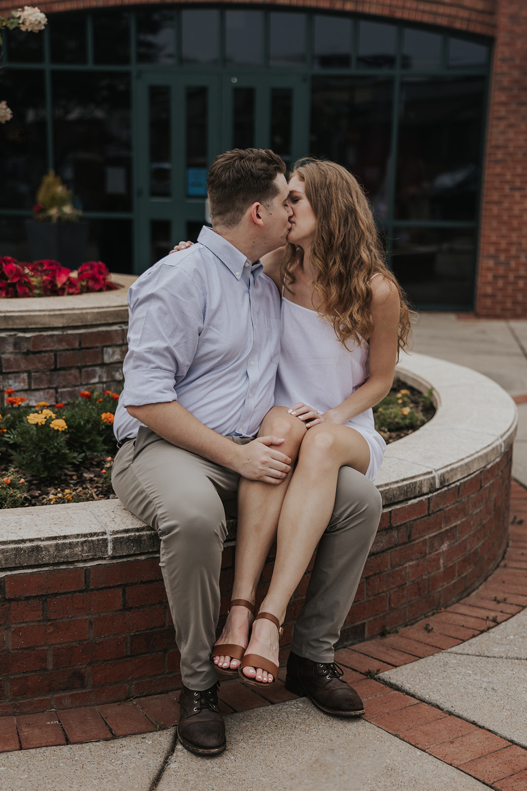 Beautiful couple sit together on an edge with yellow and red flowers in the background. A simple and easily replicated cute couple photo idea!