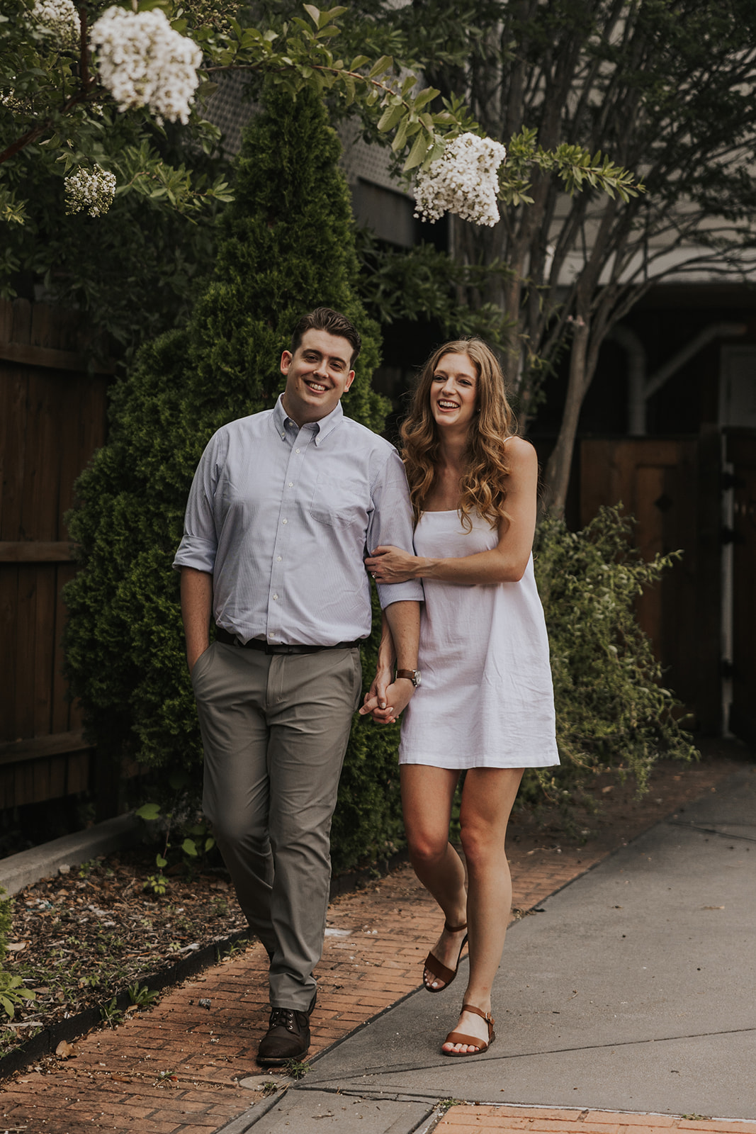 Stunning couple walk together in front of a simple wooden fence.