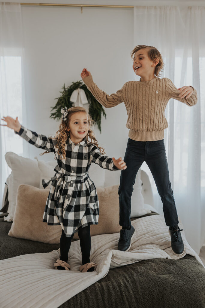 Brother and sister jump on a couch during their studio Christmas session
