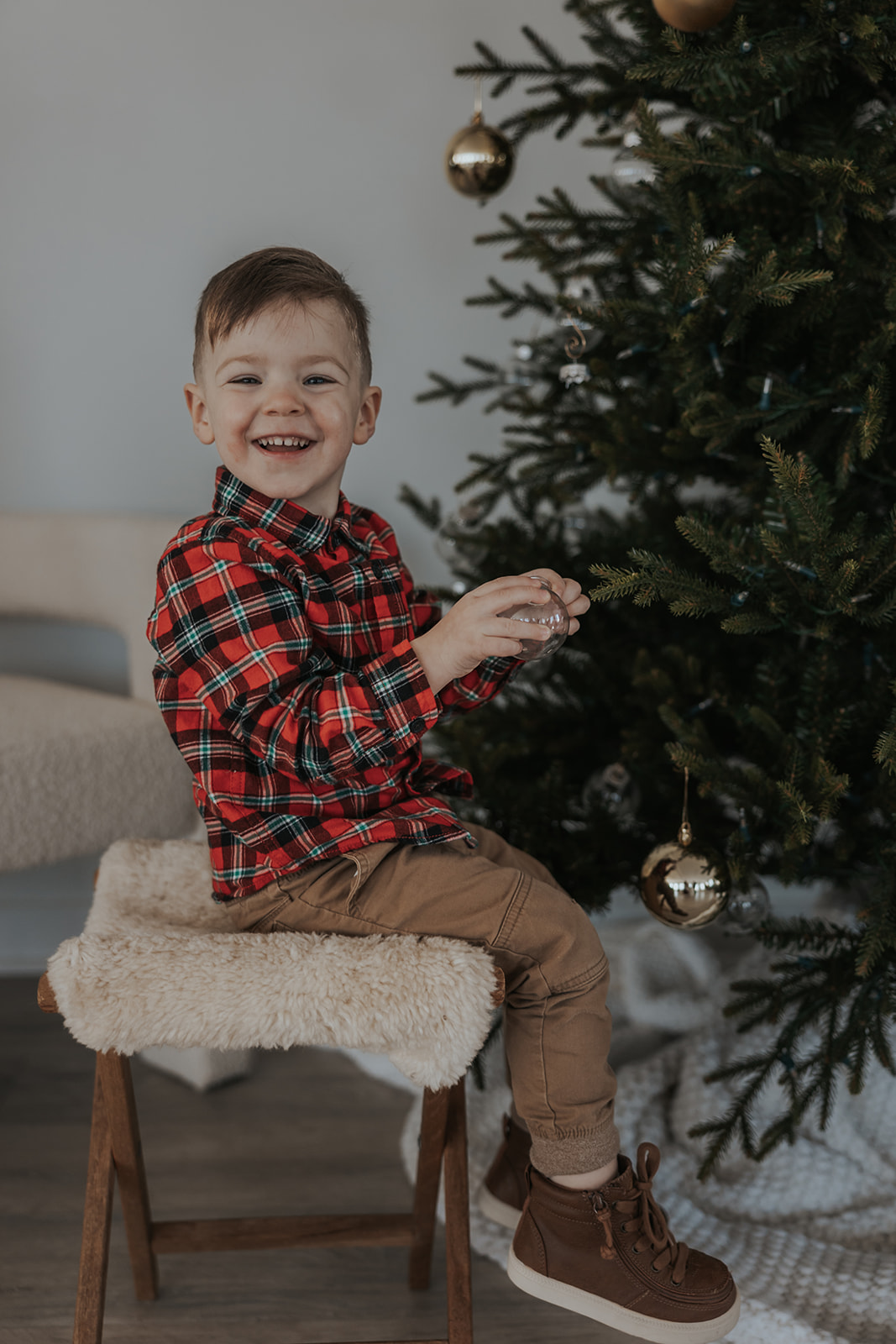 Boy in flannel shirt enjoys the Christmas tree during his families Christmas photoshoot