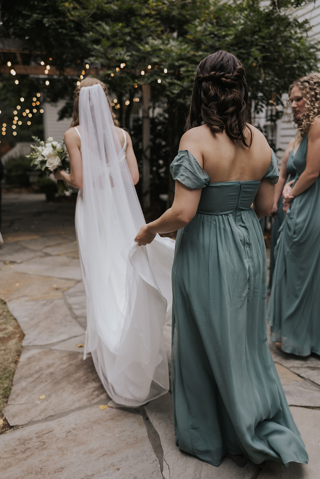 Bridesmaid carries the hem of the brides dress as they walk towards the ceremony