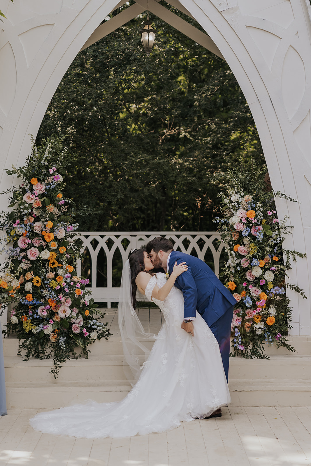 bride and groom share a kiss with their beautiful floral wedding arch in the background