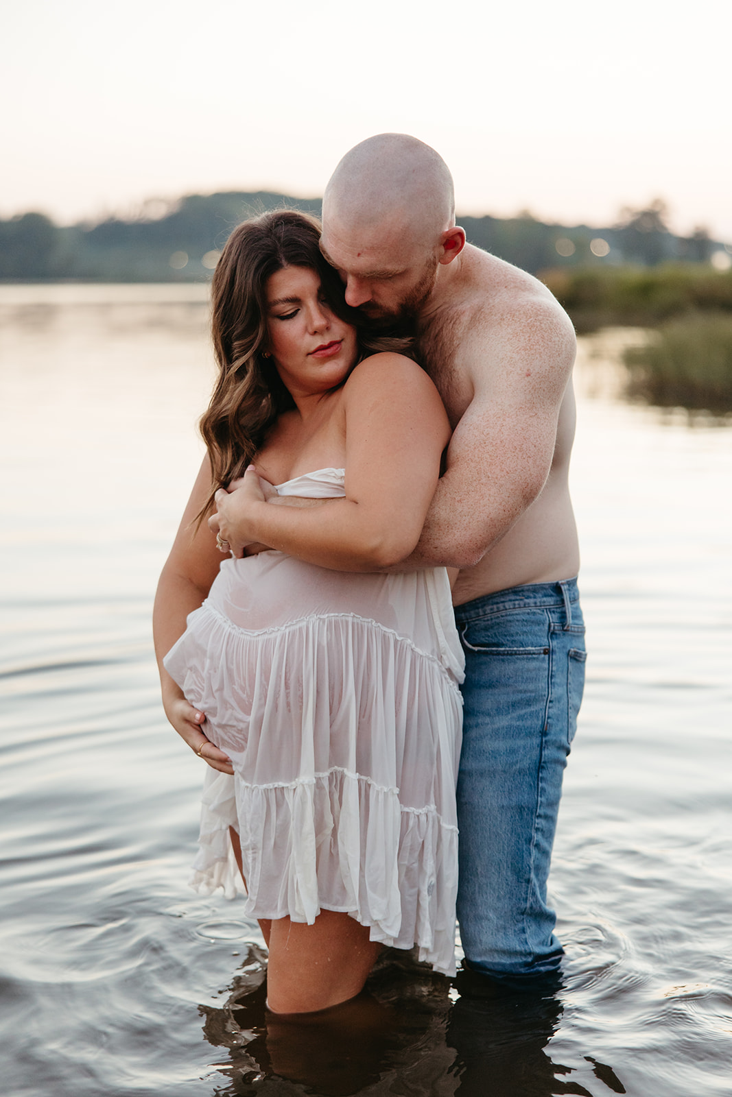 future parents pose together for a photo in the lake