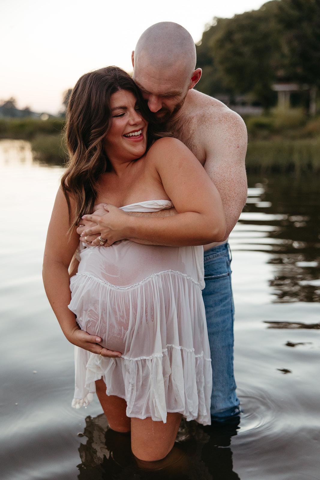 future parents pose together for a photo in the lake