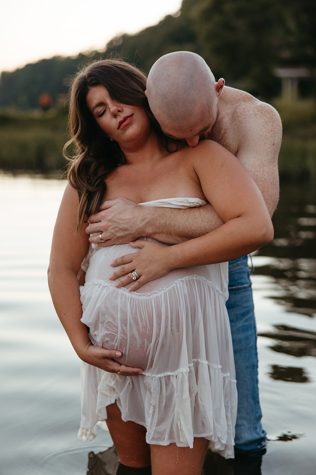 future parents pose together for a photo in the lake