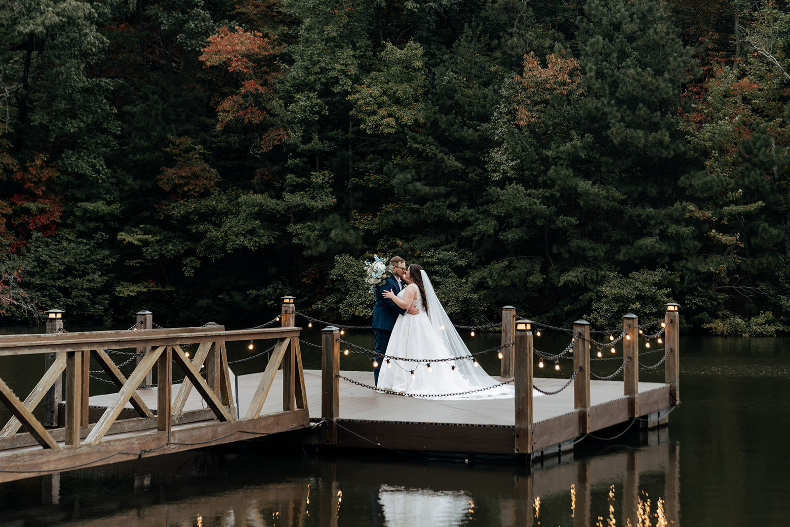 bride and groom share a kiss on a dock together after their wedding day at In The Woods