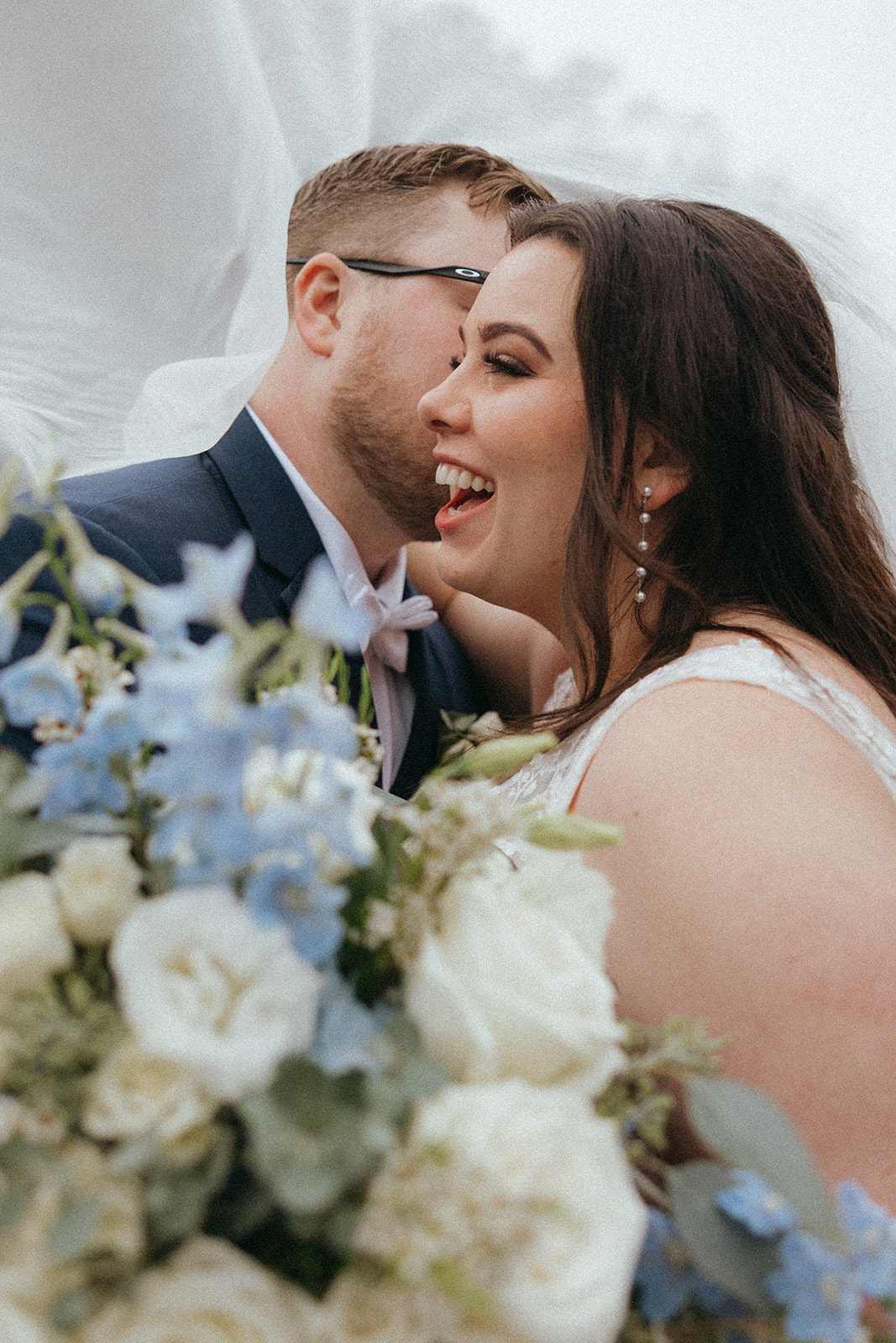 bride and groom laugh under her veil after their forest wedding venue