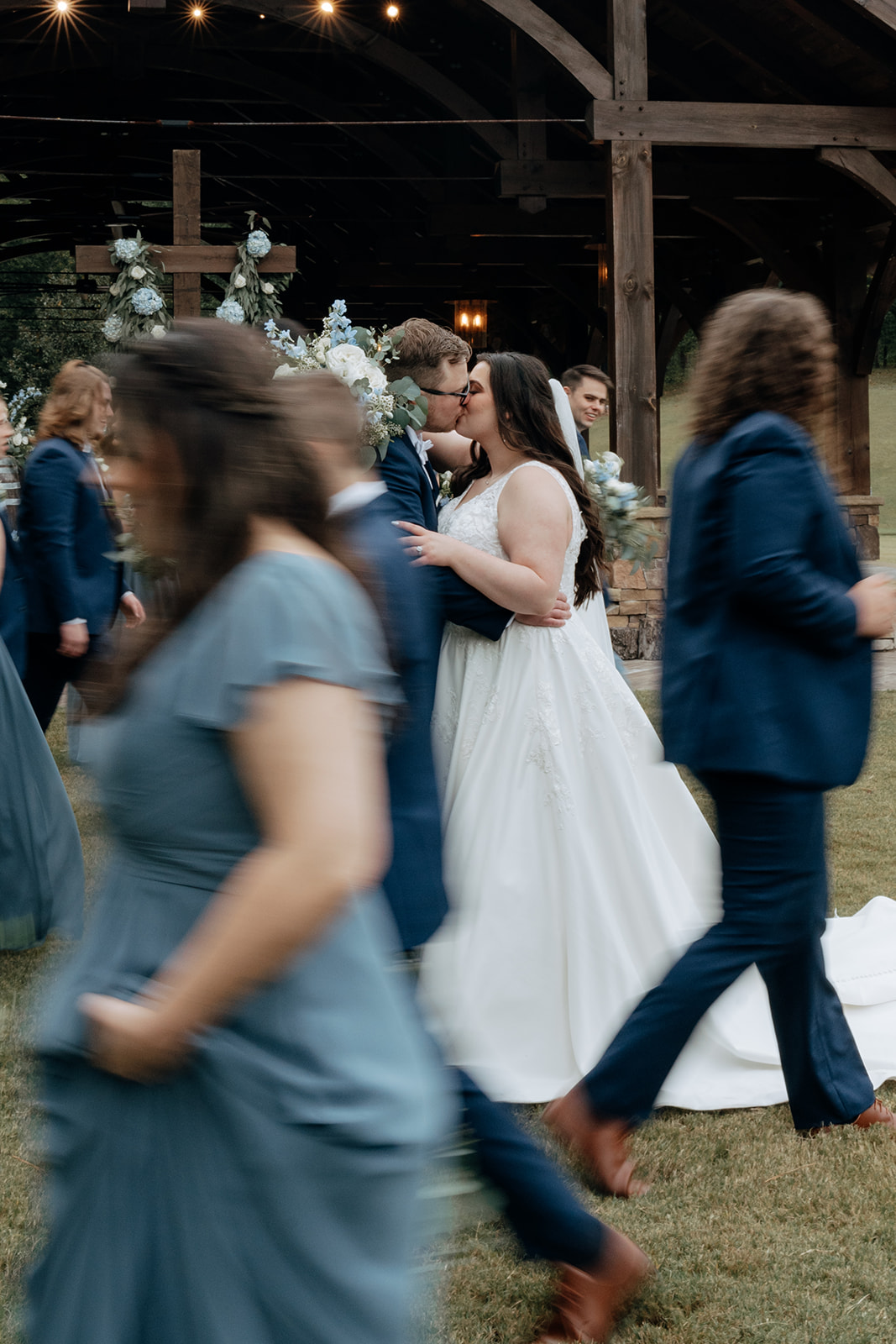 bride and groom share a kiss while their wedding party walks around them