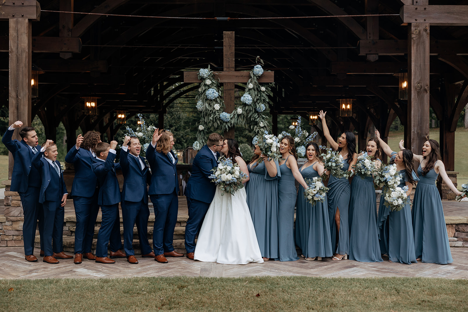 bride and groom share a kiss while their wedding party cheer them on