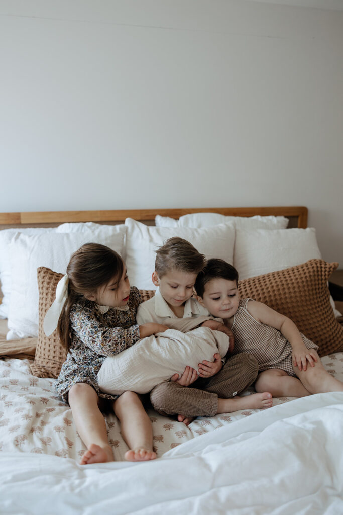 three siblings cuddle on the house with their newborn baby brother