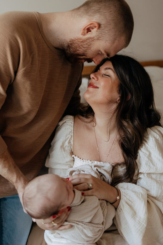 husband and wife embrace each other during newborn photoshoot