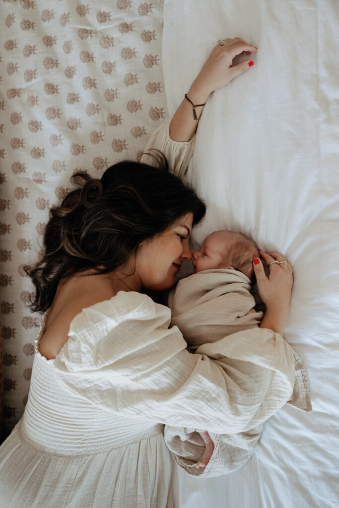 mother lays on bed with her newborn baby