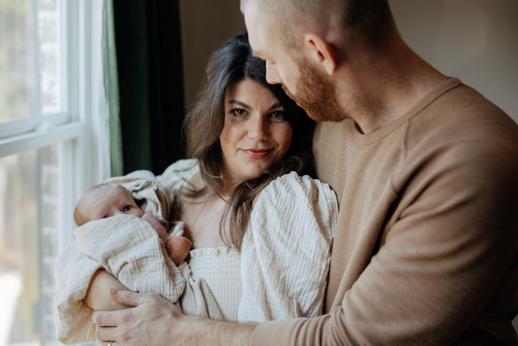 mother and father embrace each other during newborn photoshoot