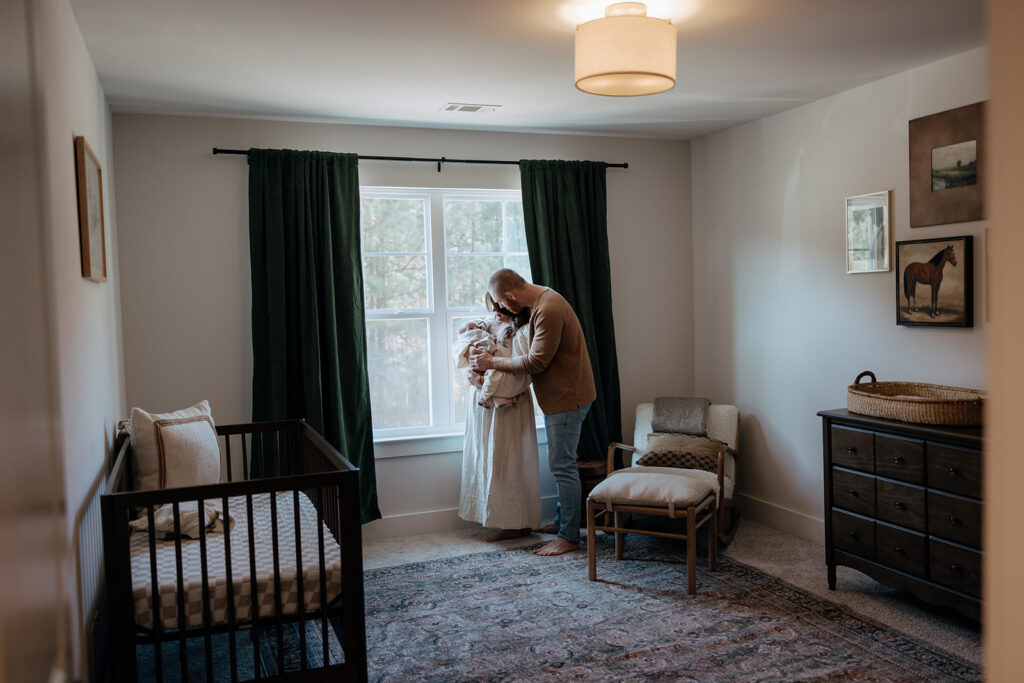 mother and father stand in nursery with their new born baby