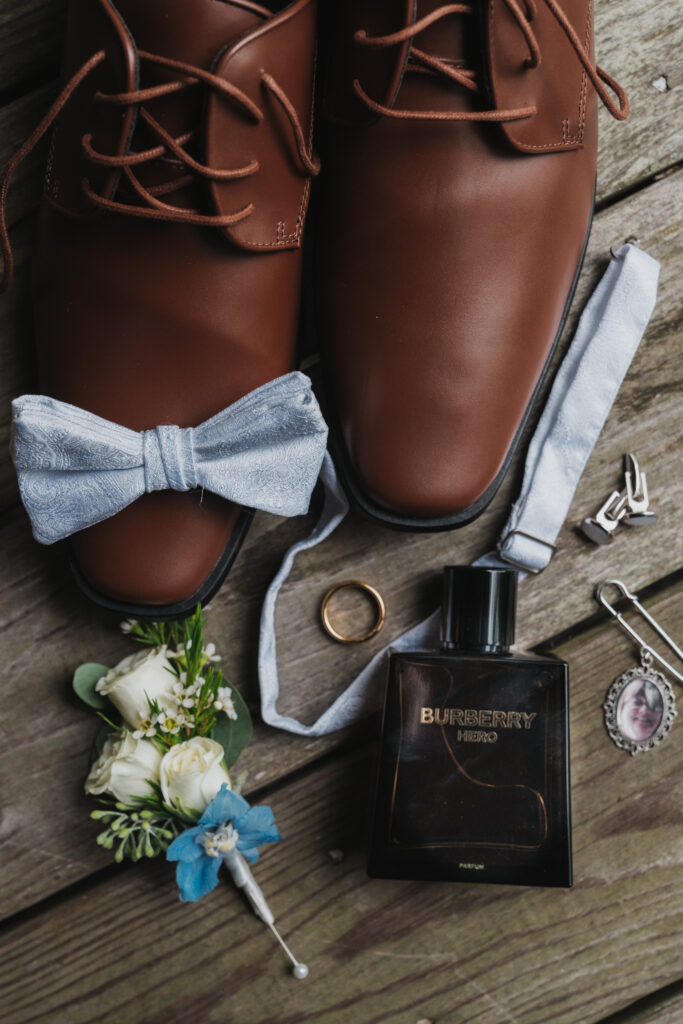 grooms wedding shoes, wedding ring, boutonniere, and cologne bottle laying on the floor
