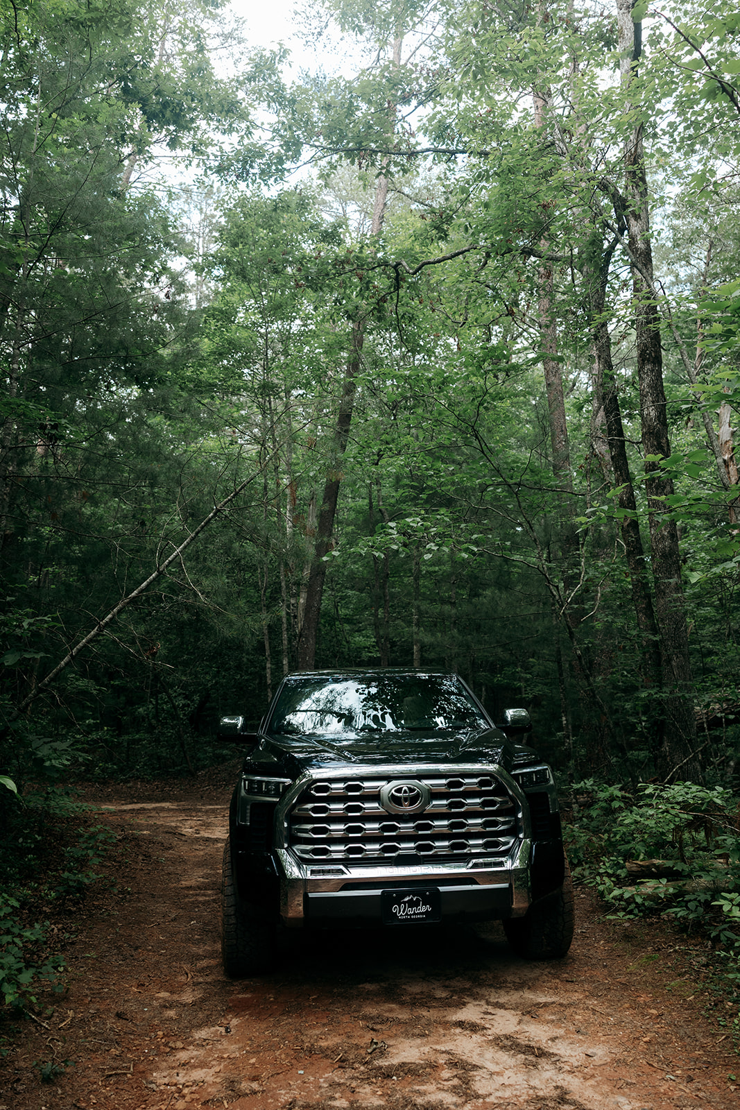 black Toyota Tundra sits under the trees with the red clay Georgia mud marking the trail