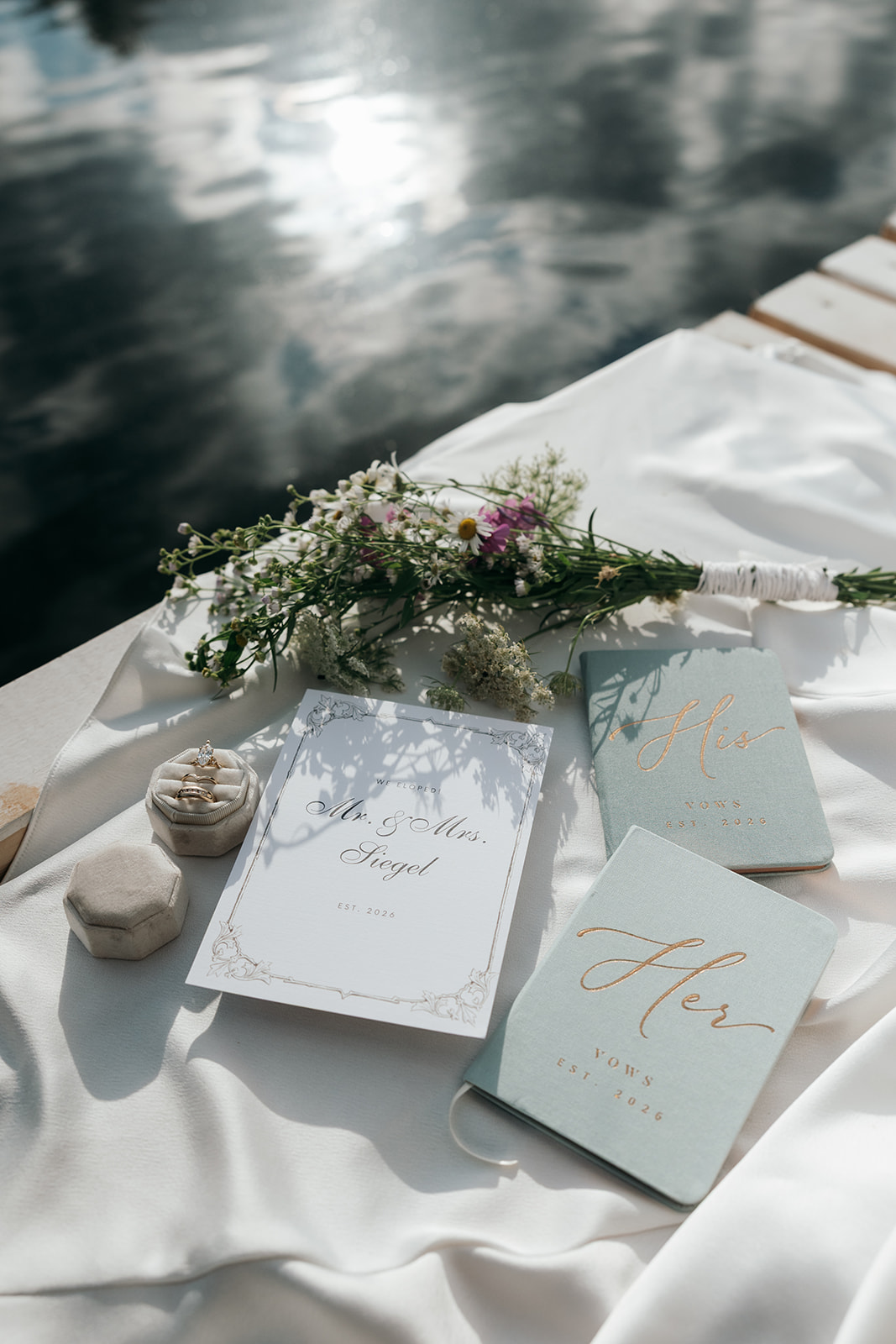 flatlay wedding details laid on a white sheet on the dock