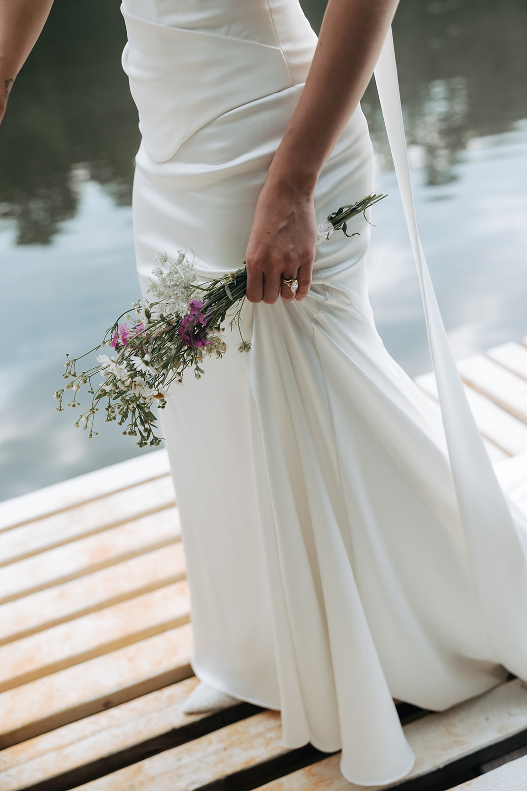 bride carries her bouquet as they walk down the dock